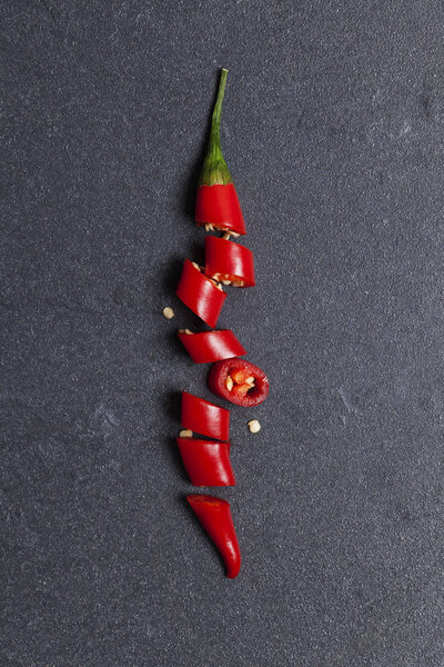 Red fresh chili pepper chopped into pieces on a dark slate backg
