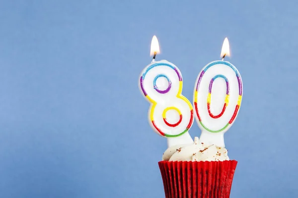 Número 80 vela de cumpleaños en un cupcake sobre un fondo azul —  Fotos de Stock