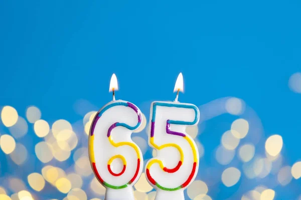 Number 65 birthday celebration candle against a bright lights an — Stock Photo, Image