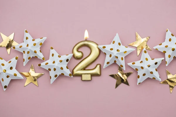 Número 2 vela de ouro e estrelas em um fundo rosa pastel — Fotografia de Stock