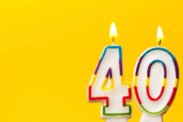 Number 40 birthday celebration candle against a bright yellow ba