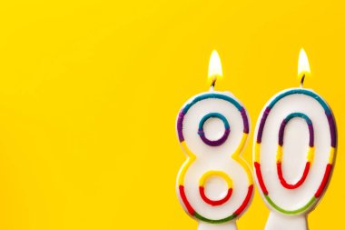 Number 80 birthday celebration candle against a bright yellow ba clipart