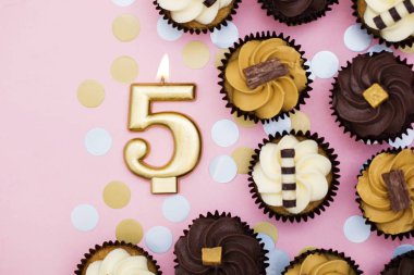 Bir pastel pembe backgro karşı cupcakes ile Sayı 5 altın mum