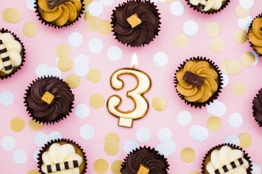 Bir pastel pembe backgro karşı cupcakes ile Sayı 3 altın mum