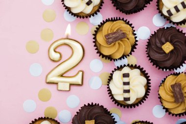 Bir pastel pembe backgro karşı cupcakes ile Sayı 2 altın mum