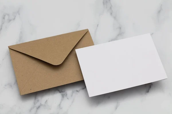 Cartão branco em branco com envelope de papel marrom kraft em mármore backg — Fotografia de Stock