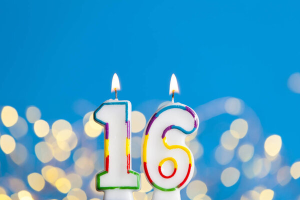 Number 16 birthday celebration candle against a bright lights an