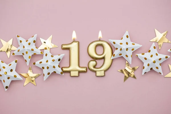 Číslo 19 zlaté svíčky a hvězdy na pastelově růžovém pozadí — Stock fotografie