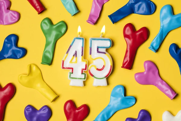 Number 45 candle with party balloons on a bright yellow backgrou — Stock Photo, Image