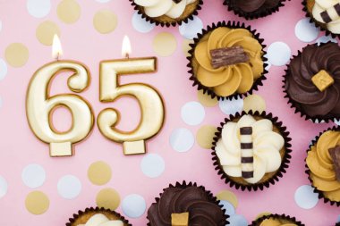 Bir pastel pembe backgr karşı cupcakes ile Sayı 65 altın mum