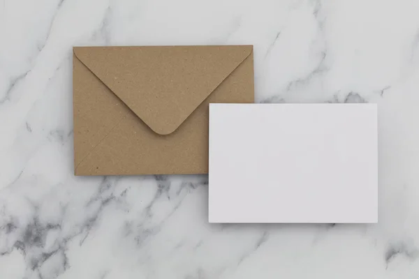 Cartão branco em branco com envelope de papel marrom kraft em mármore backg — Fotografia de Stock