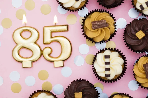 Número 85 vela de oro con cupcakes contra un fondo rosa pastel —  Fotos de Stock
