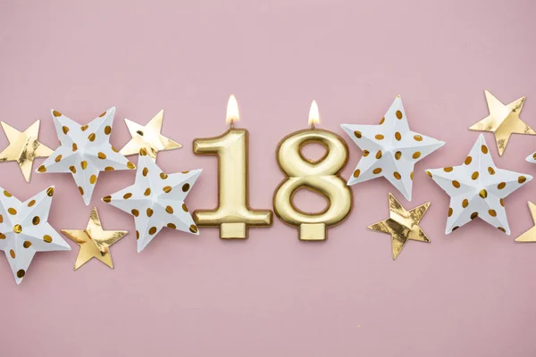 Número 18 vela de ouro e estrelas em um fundo rosa pastel — Fotografia de Stock
