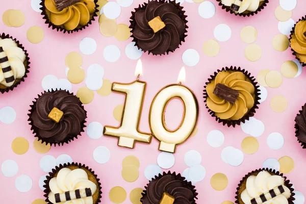 Золотая свеча номер 10 с кексами против пастельно-розового бэкгра — стоковое фото