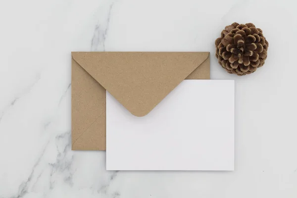 Cartão branco em branco com envelope de papel marrom kraft em mármore backg — Fotografia de Stock