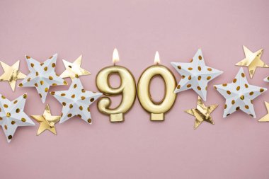 Numara 90 altın mum ve pastel pembe arka plan üzerinde yıldız