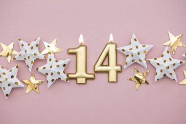 14 numara altın mum ve pastel pembe arka plan üzerinde yıldız