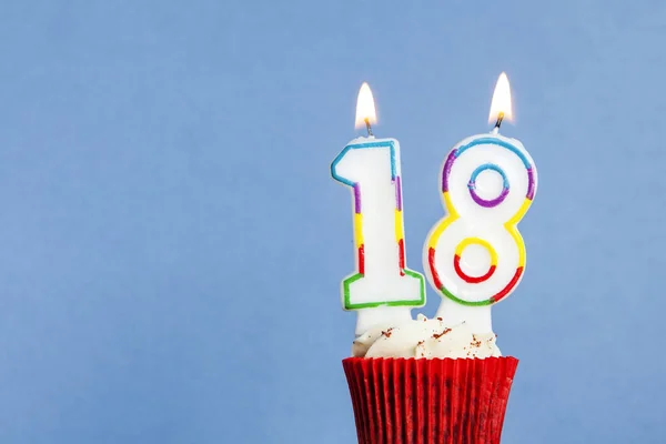 Número 18 vela de aniversário em um cupcake contra um fundo azul — Fotografia de Stock