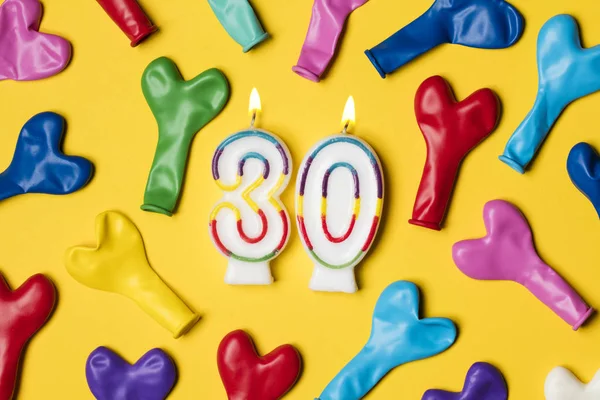 Vela número 30 con globos de fiesta sobre un fondo amarillo brillante —  Fotos de Stock