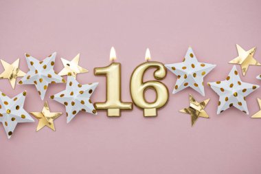 16 numara altın mum ve pastel pembe arka plan üzerinde yıldız