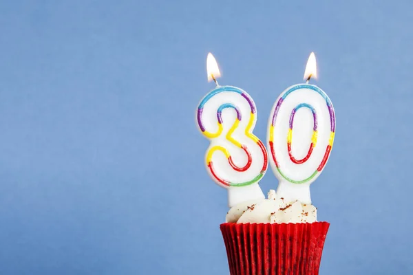 Número 30 vela de aniversário em um cupcake contra um fundo azul — Fotografia de Stock