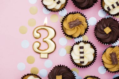 Bir pastel pembe backgro karşı cupcakes ile Sayı 3 altın mum