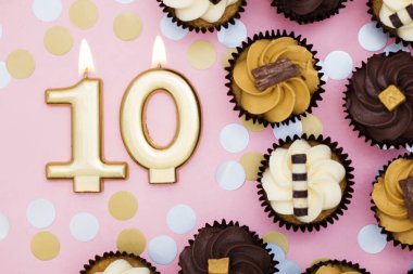 Bir pastel pembe backgr karşı cupcakes ile Sayı 10 altın mum