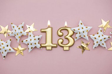 13 numara altın mum ve pastel pembe arka plan üzerinde yıldız