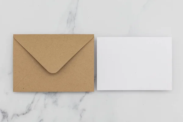 Cartão branco em branco com envelope de papel marrom kraft em mármore backg — Fotografia de Stock