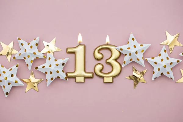 Número 13 vela de ouro e estrelas em um fundo rosa pastel — Fotografia de Stock