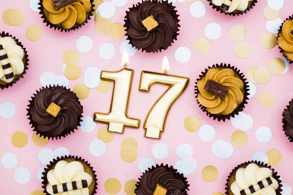 Number 17 gold candle with cupcakes against a pastel pink backgr