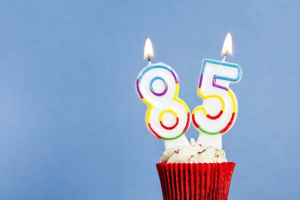 Número 85 vela de aniversário em um cupcake contra um fundo azul — Fotografia de Stock