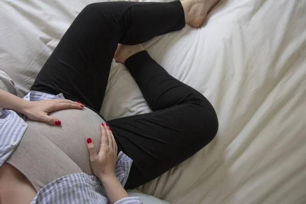 Una giovane donna incinta che riposa a casa seduta su un letto. Madre in attesa — Foto Stock