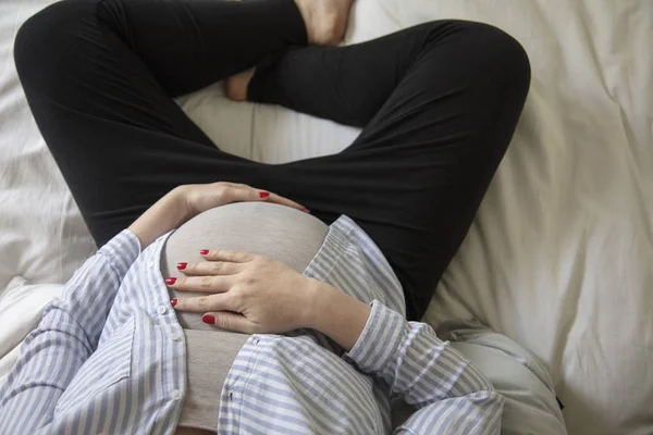 Una joven embarazada descansando en casa sentada en una cama. Madre embarazada. — Foto de Stock