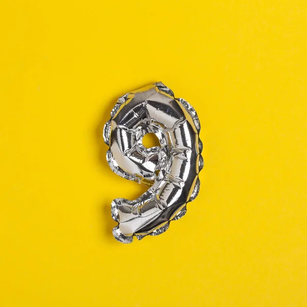 Silver foil number 9 celebration balloon on a bright yellow back — Stock Photo, Image