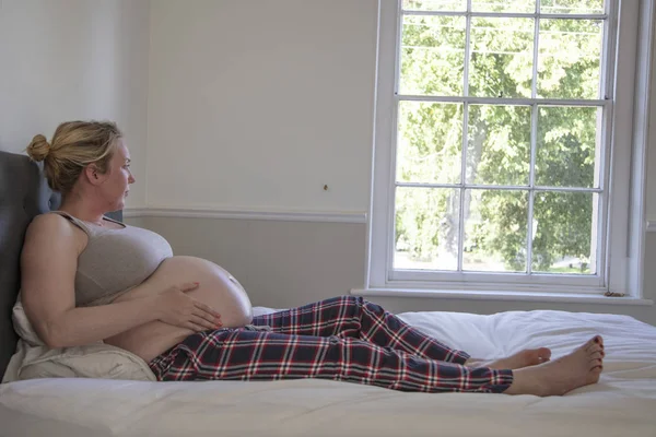 Prgnent kobieta spoczywa w łóżku trzymając jej brzuch — Zdjęcie stockowe