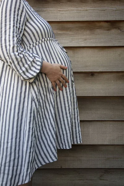 A pregnant woman holding her baby bump stood against a plain background — Stock Photo, Image