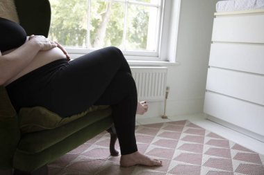 Bir sandalyede rahatlatıcı iken onun bebek yumru tutan bir prgnant kadın