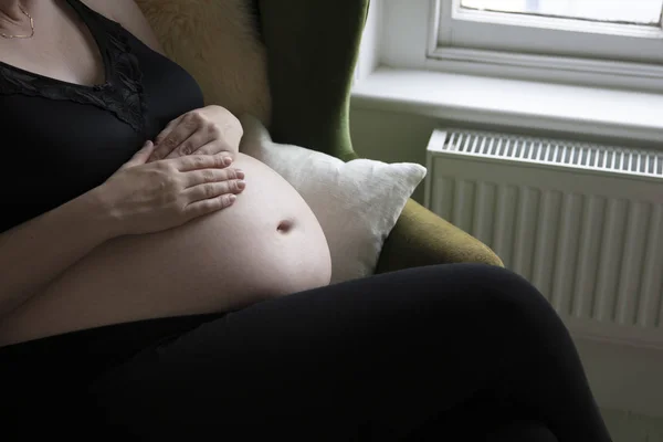 Close-up de uma mulher prgnant segurando seu bebê colisão enquanto relaxa em uma cadeira — Fotografia de Stock