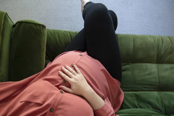 Una mujer prgnant que se relaja en un sofá verde sosteniendo su baby bump — Foto de Stock