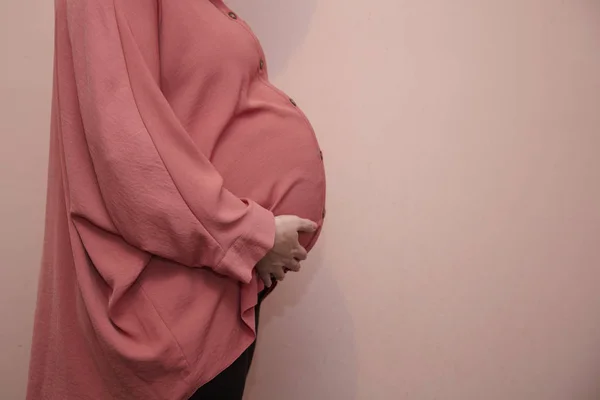 Una mujer prgnante vistiendo una camisa rosa estampada contra una pared rosa — Foto de Stock