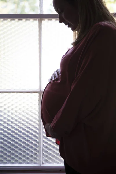 Silhouette di una donna prgnant in piedi davanti a una finestra — Foto Stock