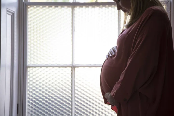 Silueta de una mujer prgnante de pie frente a una ventana — Foto de Stock