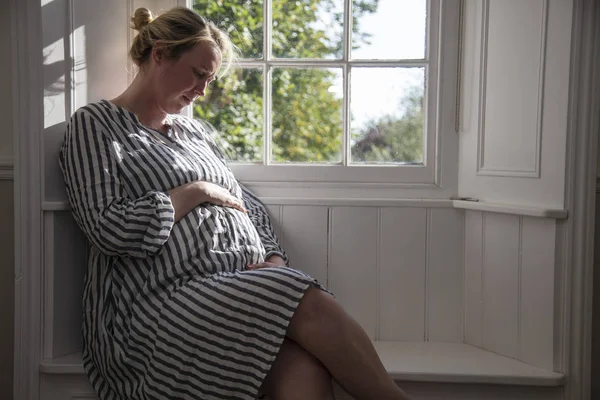 Una mujer prgnante sentada junto a una ventana —  Fotos de Stock