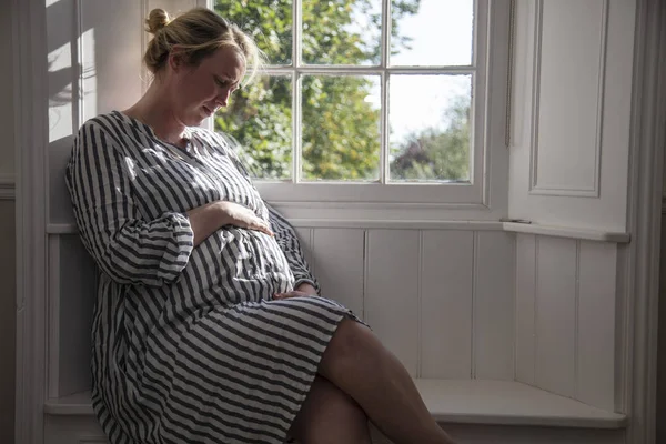 Una donna prgnante seduta vicino ad una finestra — Foto Stock