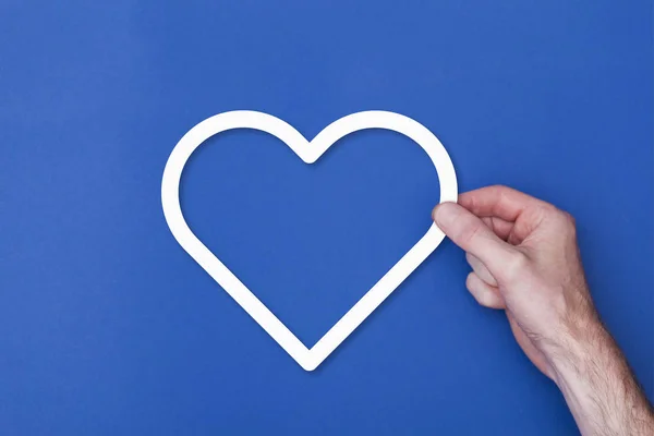 Mão masculina segurando um símbolo de ícone do coração contra um fundo azul — Fotografia de Stock