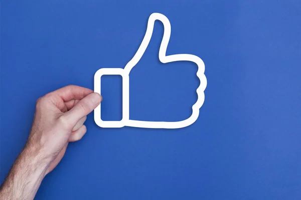 stock image male hand holding a thumbs up icon symbol against a blue backgro