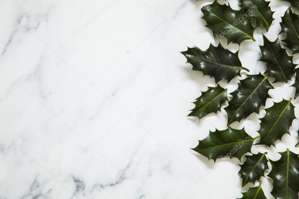 Christmas layout made from festive holly leaves on a white marbl
