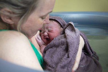 A new mother embracing her newborn baby after a natural pool home birth clipart
