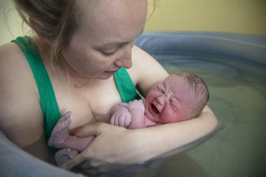 Yeni bir anne, yeni doğmuş bebeğini havuzda doğumdan sonra kucaklıyor.